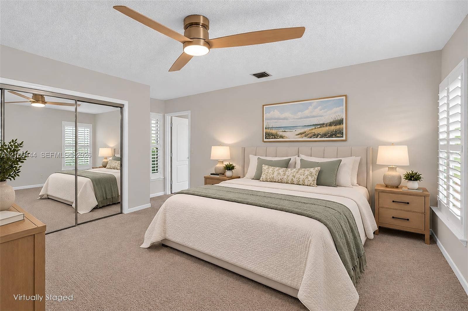 Neutral-toned interior featuring wall-to-wall carpeting, floor-to-ceiling mirrored closet doors, a brushed metal ceiling fan with integrated lighting, and white plantation shutters