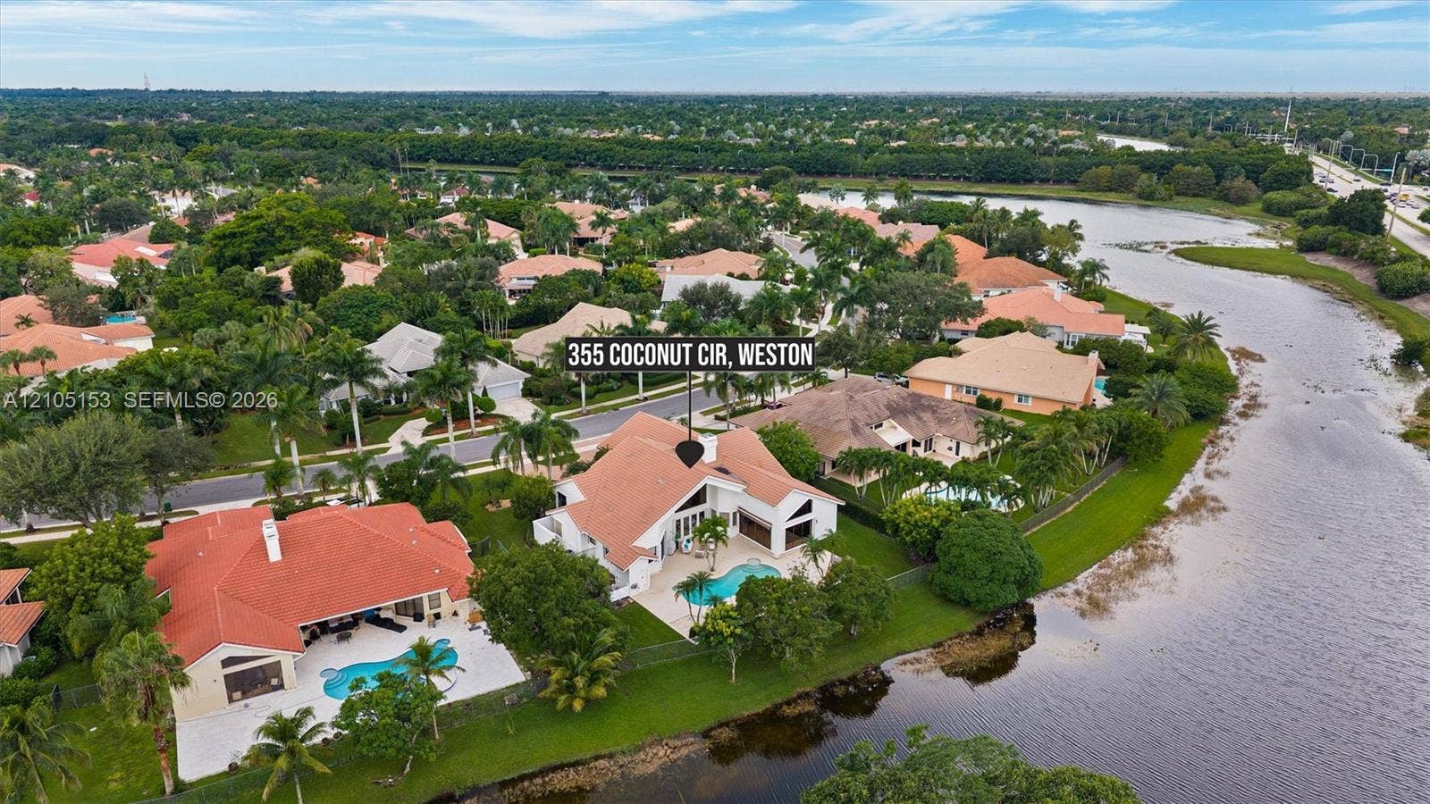 Waterfront property with a private swimming pool, terracotta tile roof, and mature landscaping