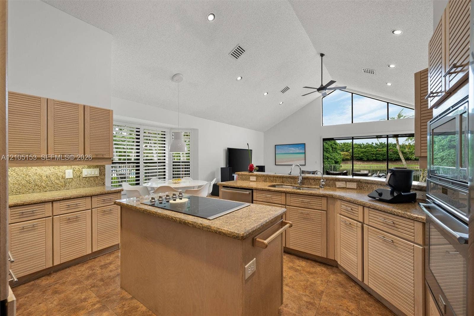 Vaulted ceiling with recessed lighting and a ceiling fan, integrated double oven, and a built-in cooktop on a central island