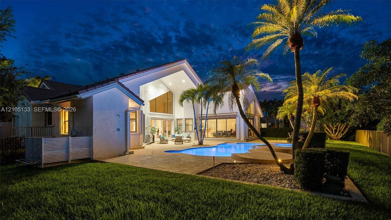 Expansive pool deck with a freeform swimming pool, mature palm trees, and a manicured lawn