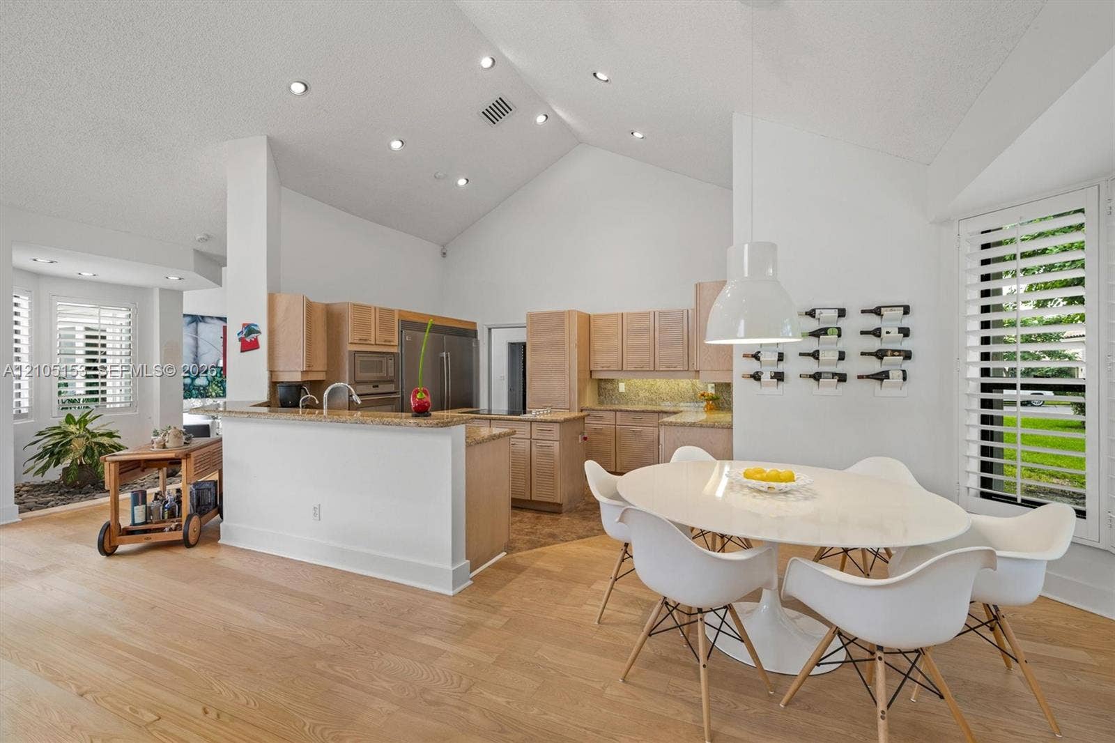 Vaulted ceilings with recessed lighting, wood-finish flooring, kitchen with light wood cabinetry, stone countertops, and stainless steel appliances