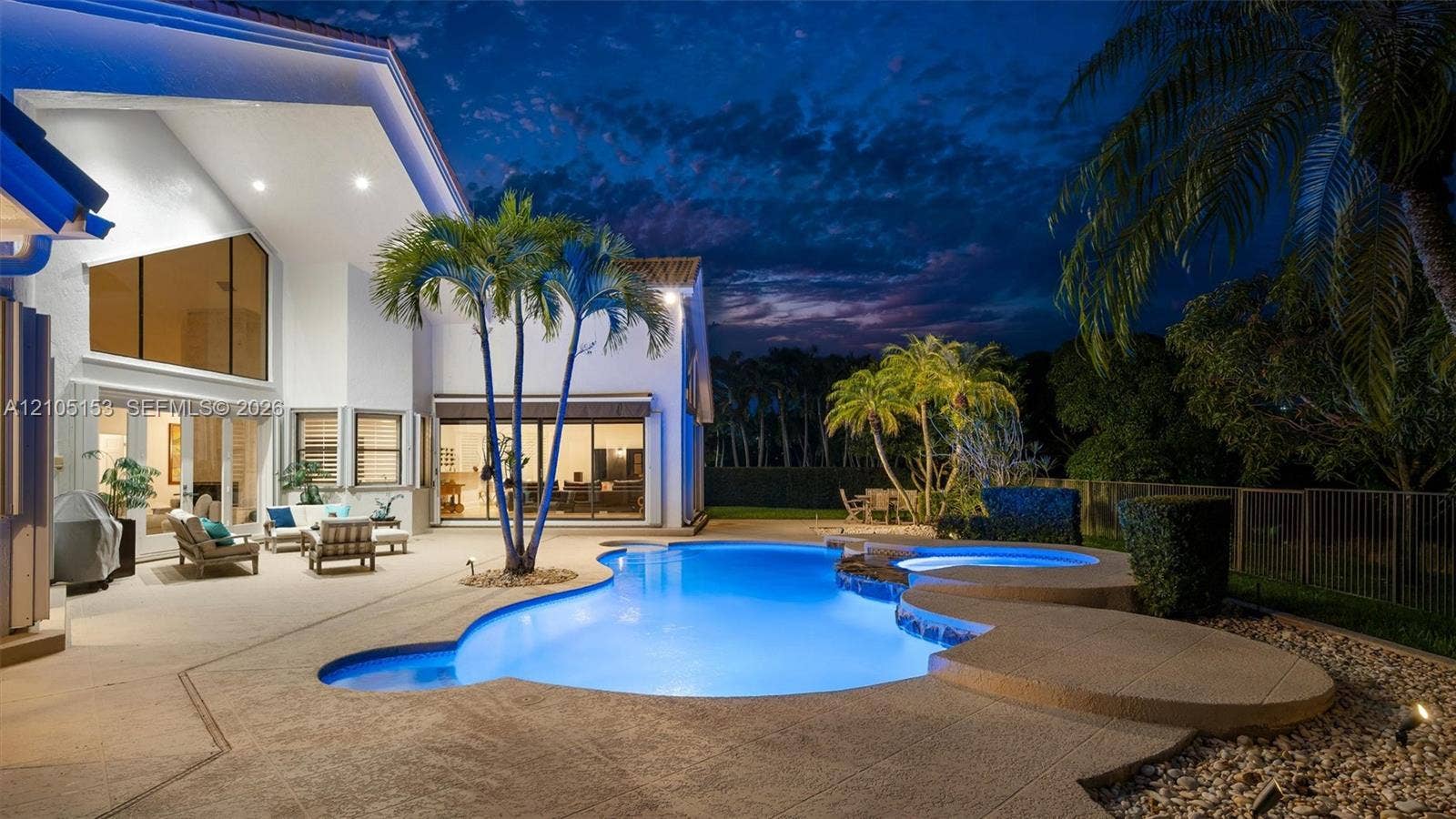 Expansive patio featuring a freeform swimming pool, integrated spa, and mature palm trees
