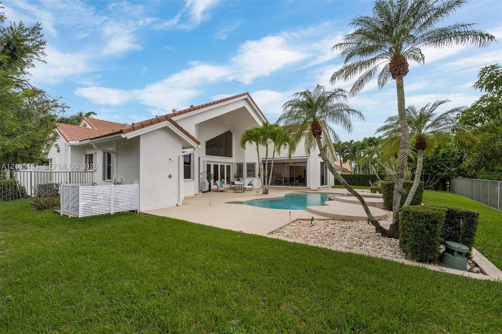 Expansive backyard featuring a manicured lawn, a freeform swimming pool, and mature palm trees