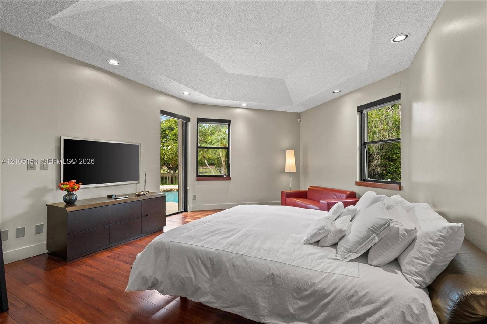 Hardwood flooring, tray ceiling with recessed lighting, built-in media console, sliding glass door, and multiple windows