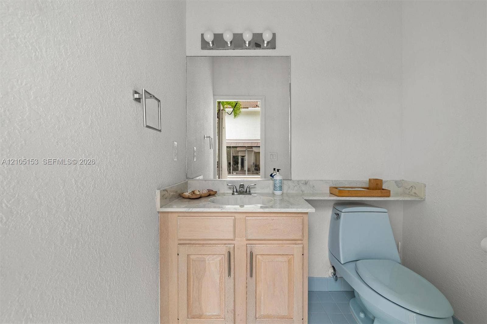 Vanity with a light wood-finish cabinet and stone-look countertop, a large wall-mounted mirror, and a four-bulb vanity light fixture