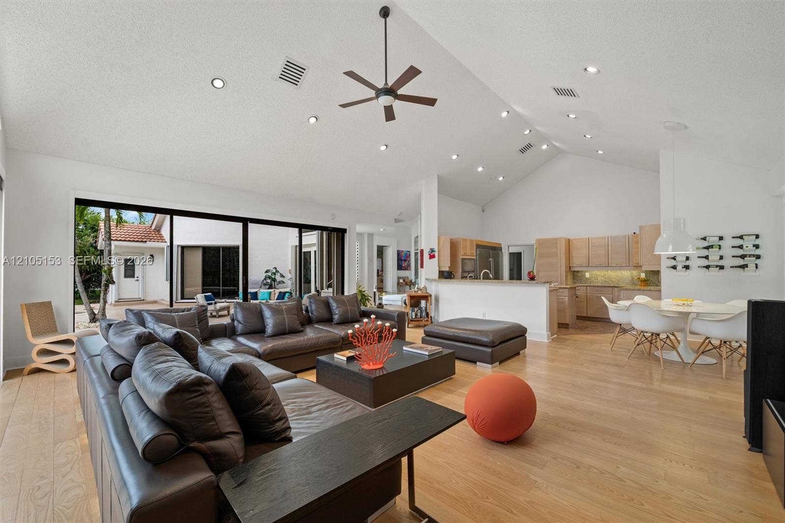 Open-concept living area featuring vaulted ceilings, recessed lighting, wood-finish flooring, and a kitchen with wood cabinetry