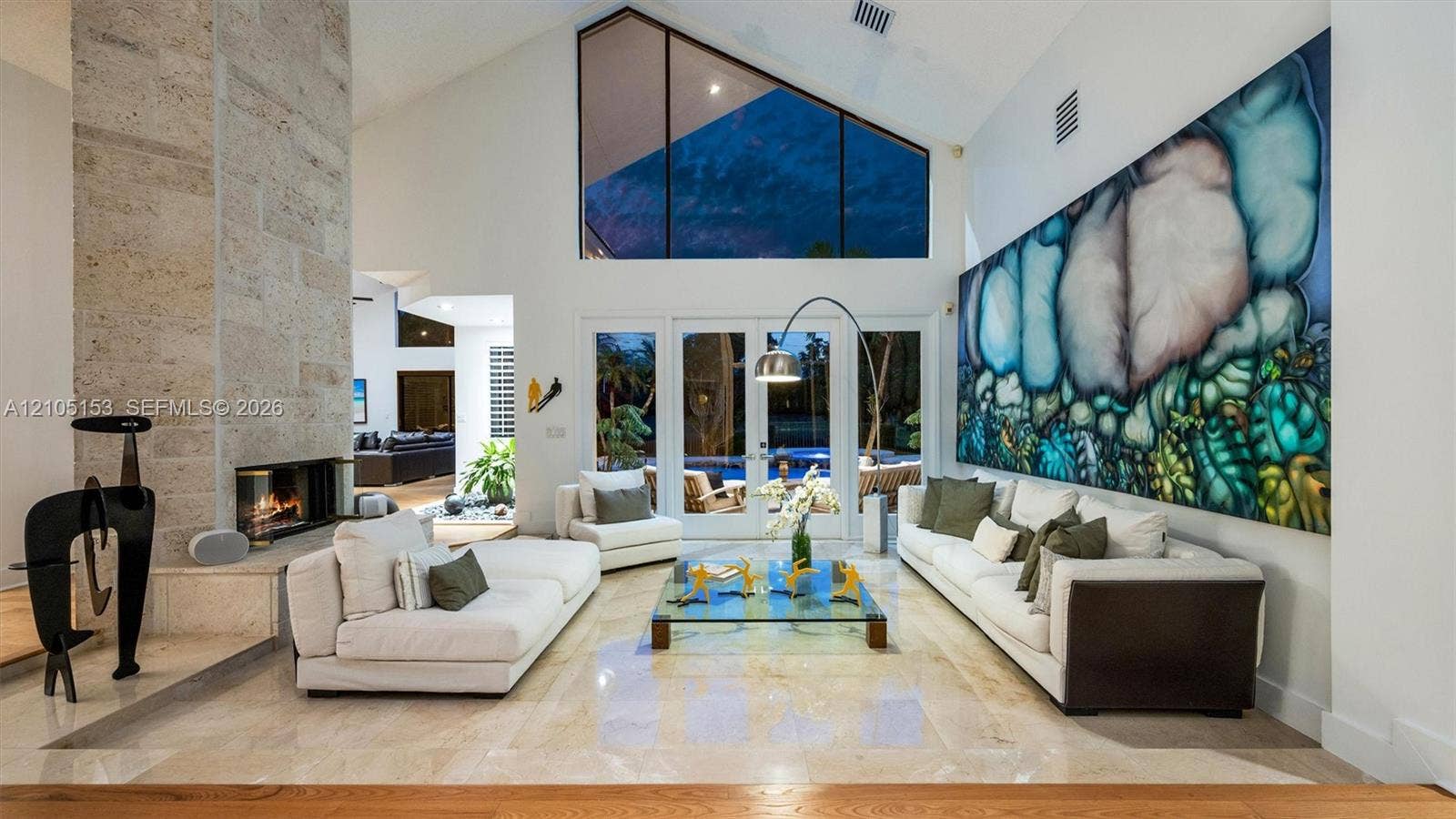 Vaulted ceiling with high windows, stone-clad fireplace, light-toned flooring, and French doors to the exterior