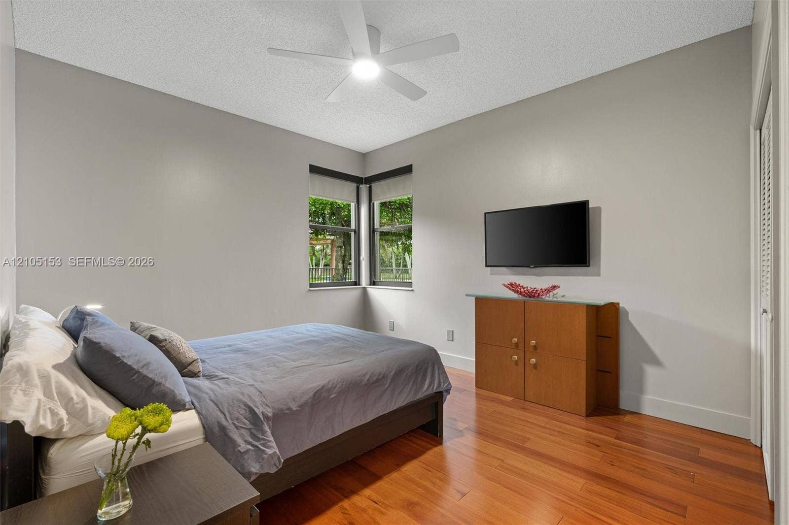 Hardwood-finish flooring, corner windows with roller shades, and a ceiling fan with integrated lighting
