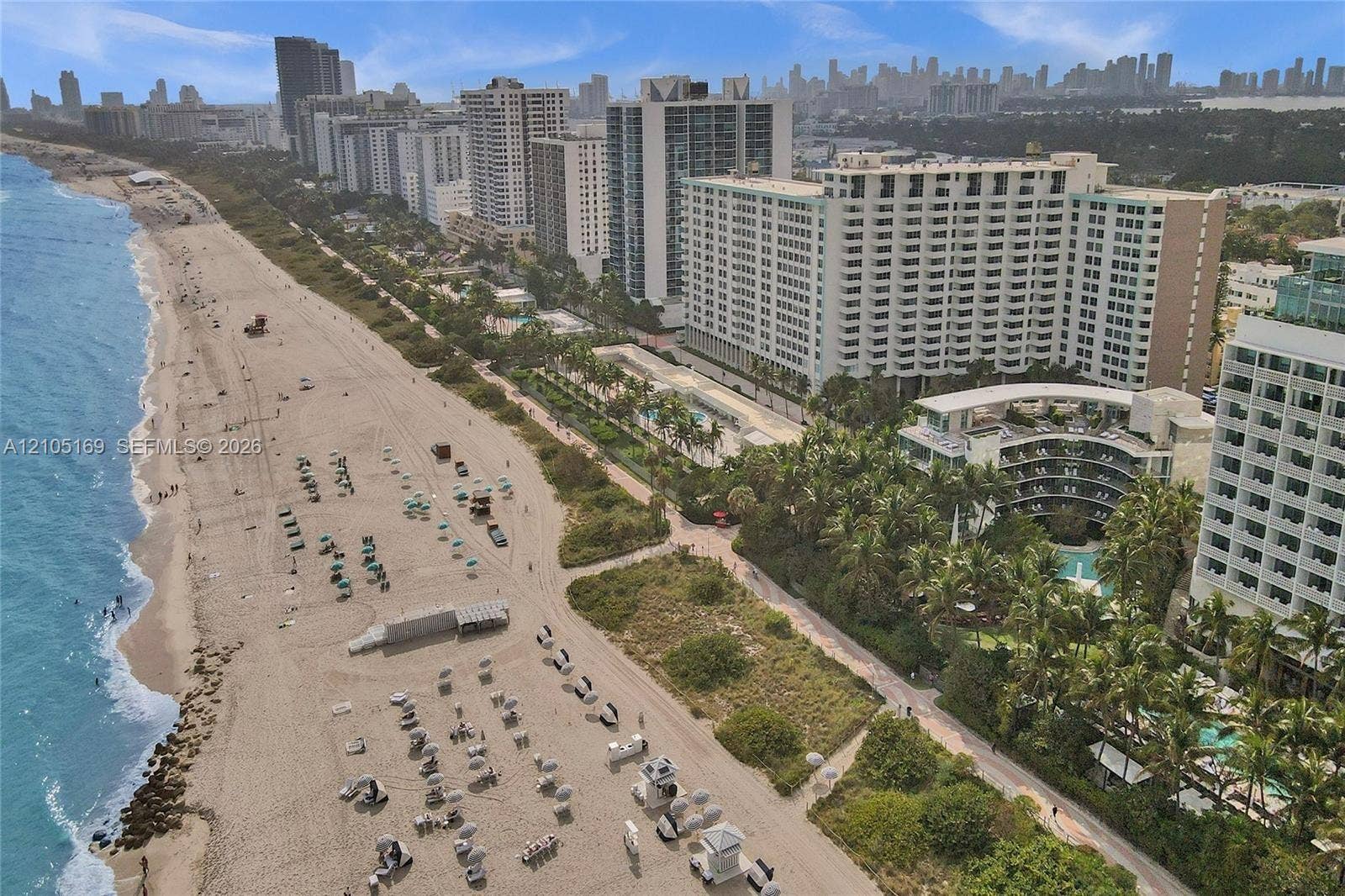 2899 Collins Avenue, #521, Miami Beach, FL 33140 Expansive sandy beach with turquoise ocean, bordered by palm trees and high-rise buildings