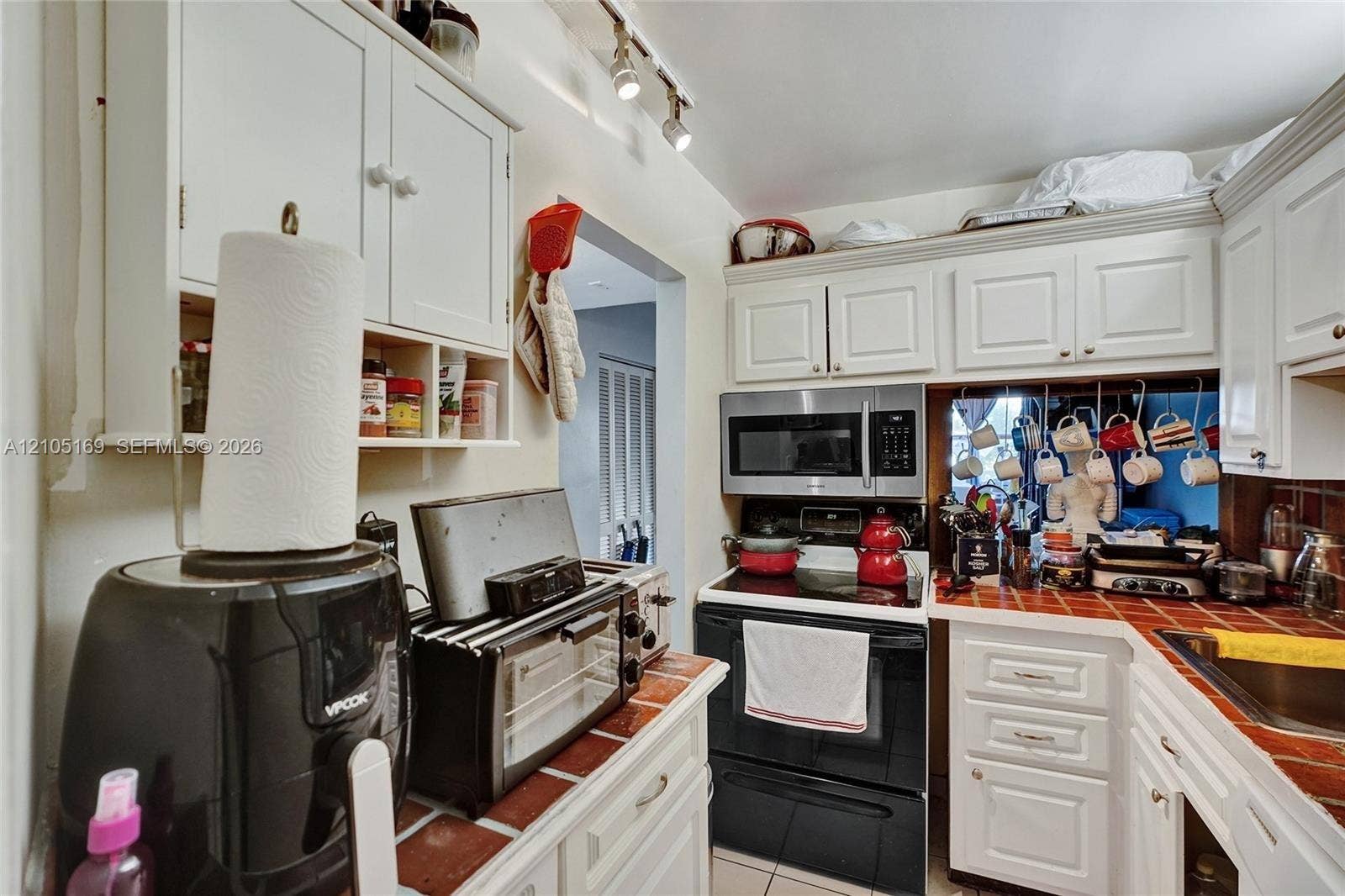 2899 Collins Avenue, #521, Miami Beach, FL 33140 White cabinetry, stainless steel microwave, track lighting, tiled countertop, and stainless steel sink