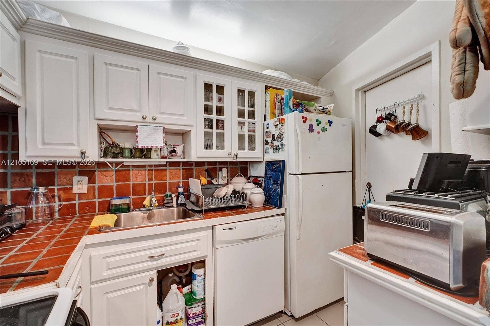 2899 Collins Avenue, #521, Miami Beach, FL 33140 White cabinetry with glass-front accents, stainless steel sink, and a red tile backsplash