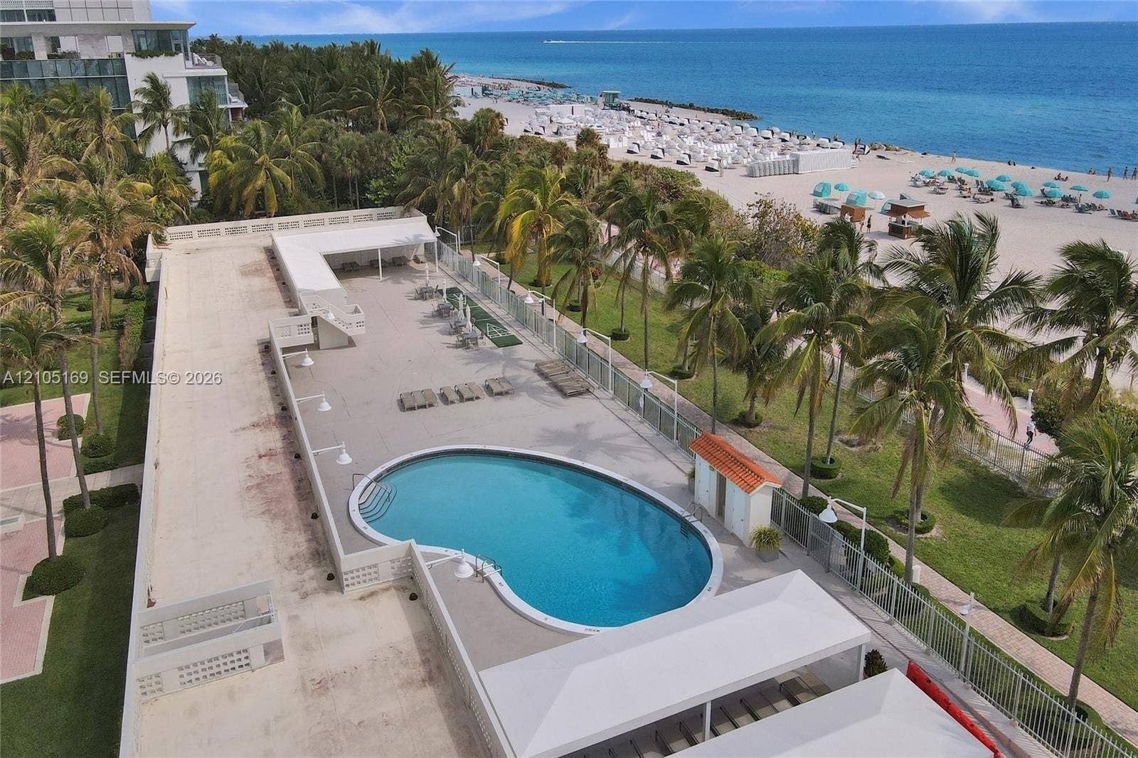 2899 Collins Avenue, #521, Miami Beach, FL 33140 Outdoor swimming pool, paved pool deck, lush landscaping with palm trees, direct beach access, and oceanfront location