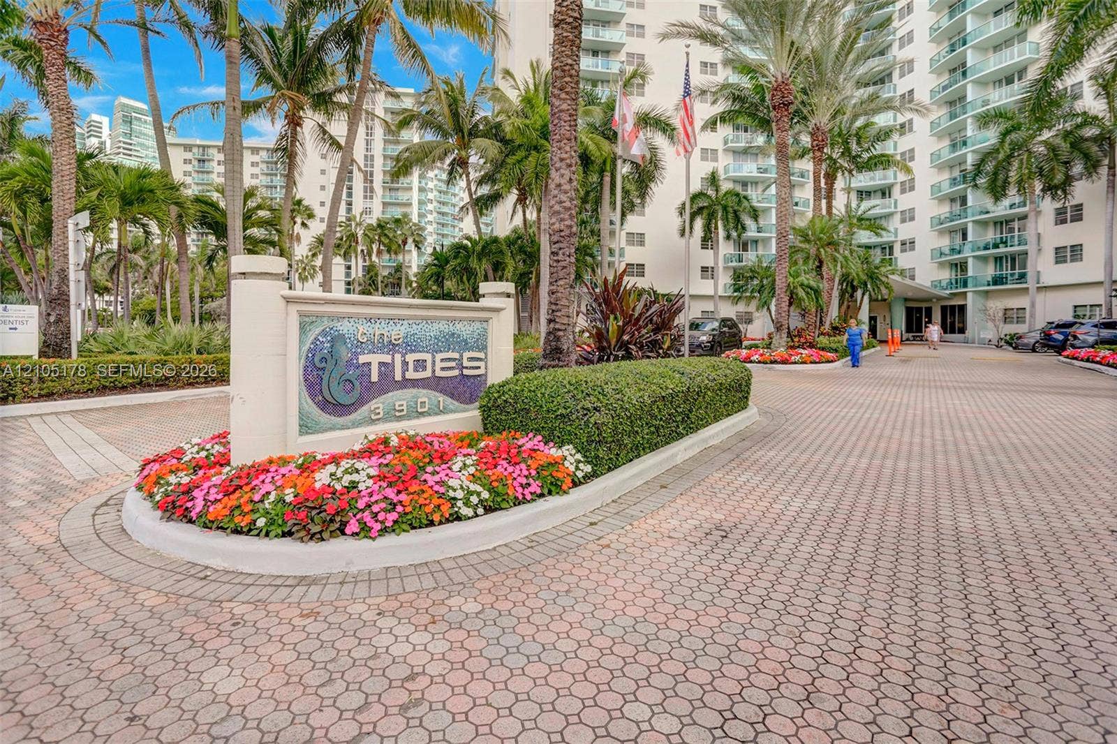 3801 S Ocean Drive, #10G, Hollywood, Hollywood, FL 33019 Paver driveway entrance featuring mature palm trees, manicured hedges, and floral landscaping surrounding the property monument sign