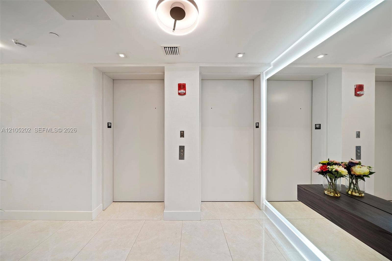 Dual elevator lobby featuring large-format tile flooring, recessed ceiling lighting, and a full-length wall mirror