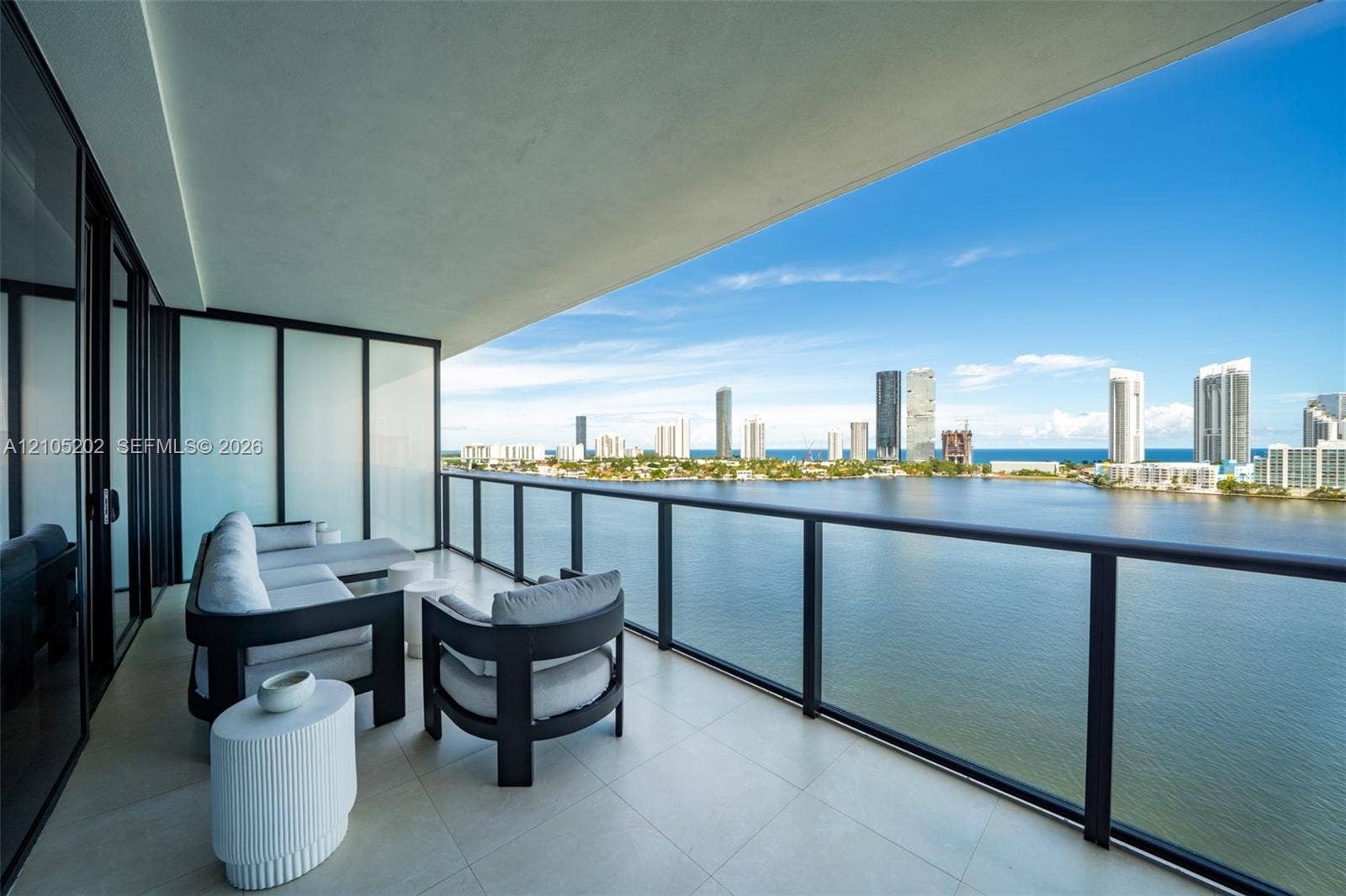 Covered balcony with large-format tile flooring, black metal railing, and expansive water and urban skyline backdrop