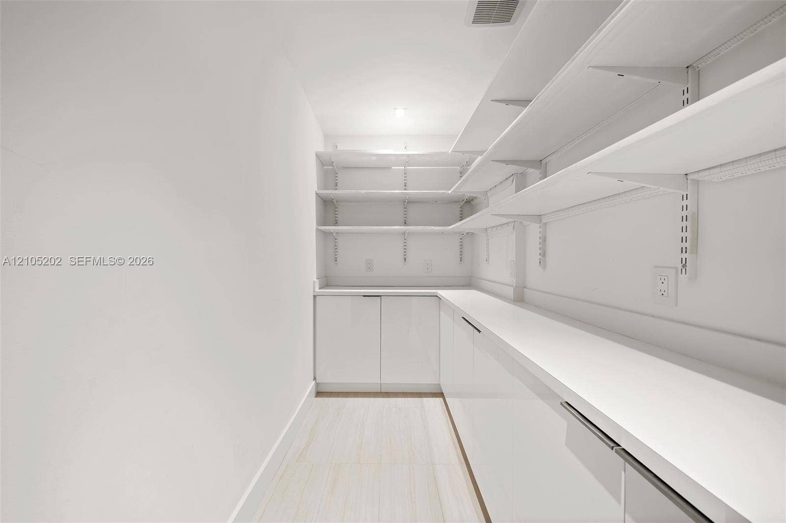 Storage area featuring floor-to-ceiling adjustable shelving, extensive solid-surface countertops, high-gloss cabinetry, and light-toned flooring