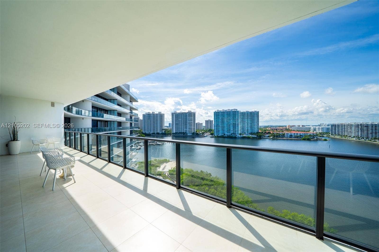 Covered wrap-around balcony with oversized neutral floor tile, glass panel railing, and metal frame