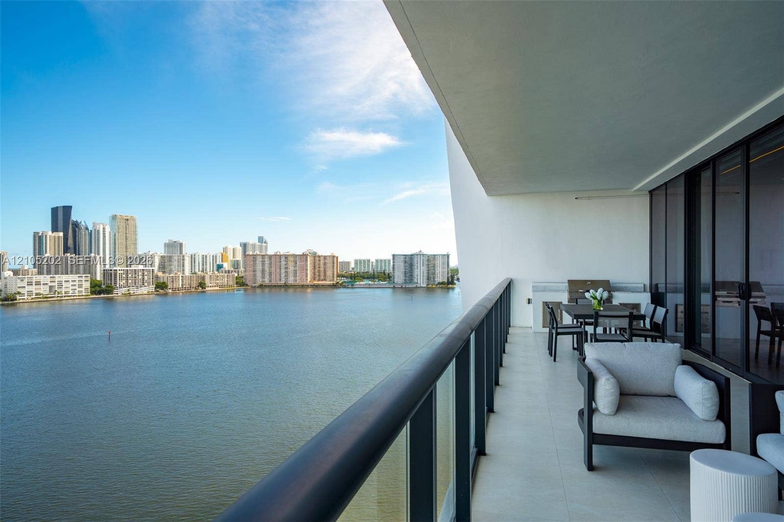 Covered balcony featuring a glass panel railing, tiled flooring, built-in outdoor kitchen, and water backdrop