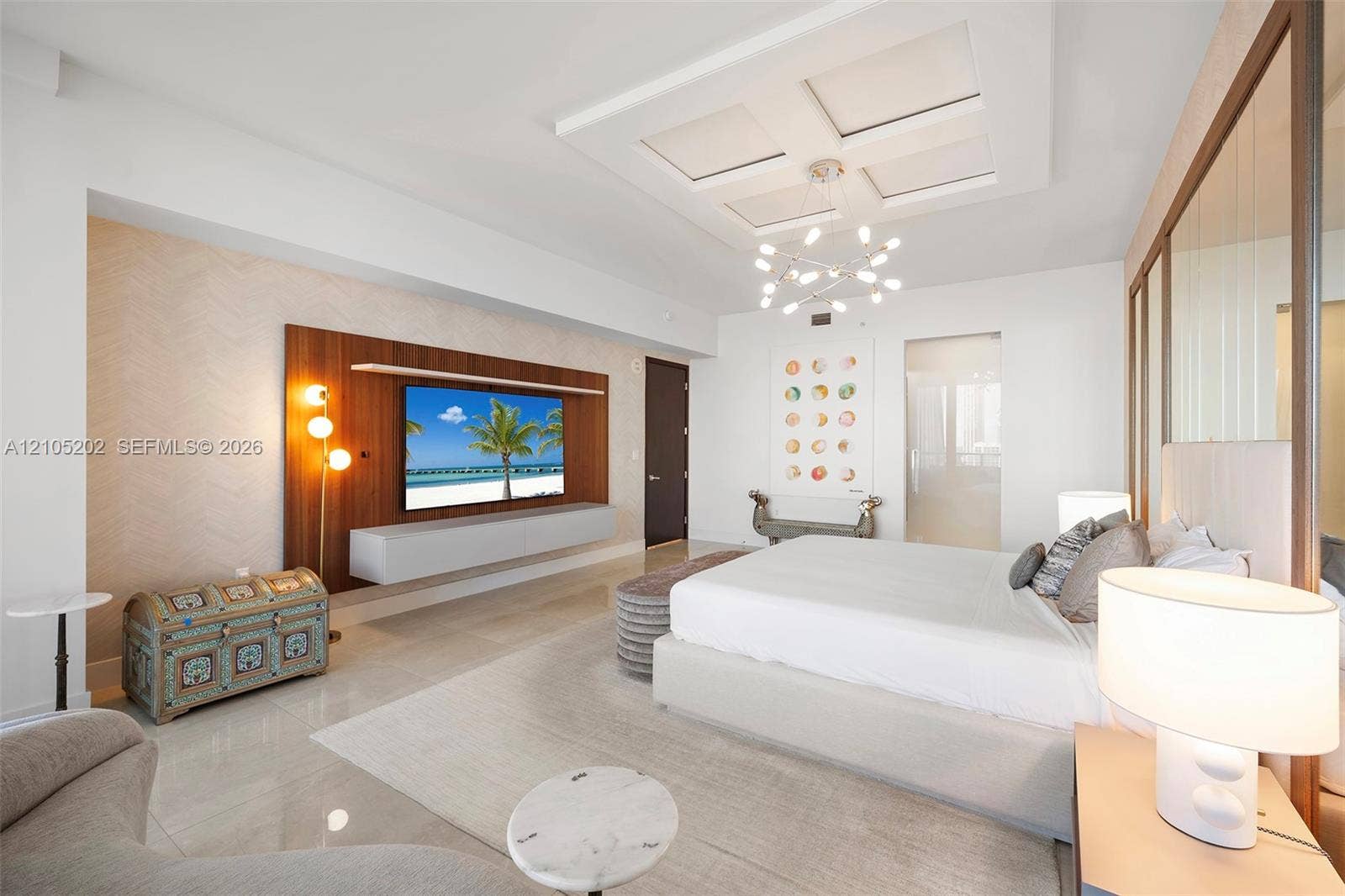 Coffered ceiling with modern multi-arm chandelier, wall-mounted wood-panel media feature, floating cabinetry, and tile flooring