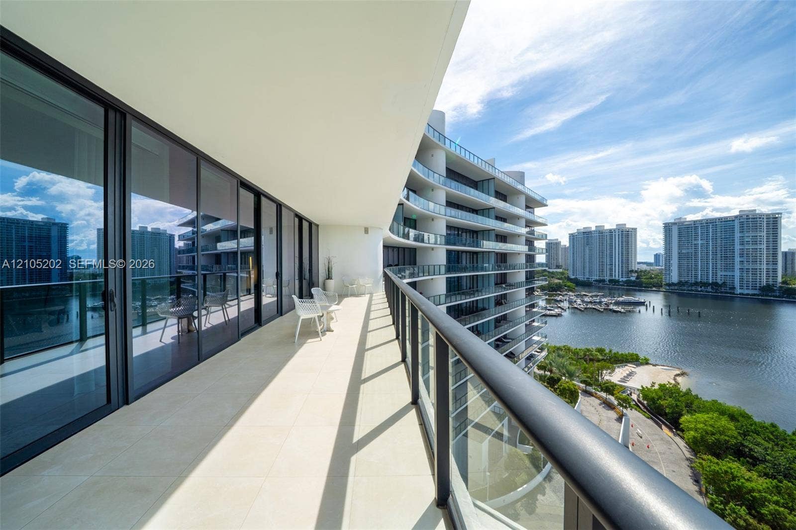 Expansive covered balcony featuring large-format tile flooring, a sleek metal and glass railing system, and floor-to-ceiling sliding glass doors