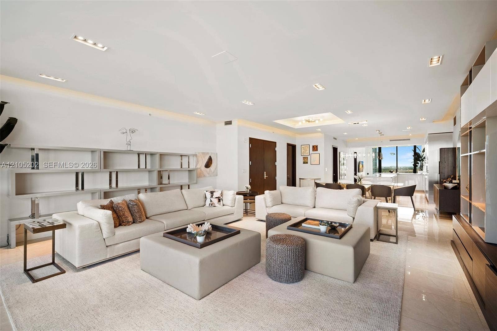 Open-concept interior featuring large-format stone flooring, recessed ceiling lighting, expansive built-in shelving, and a custom architectural media wall