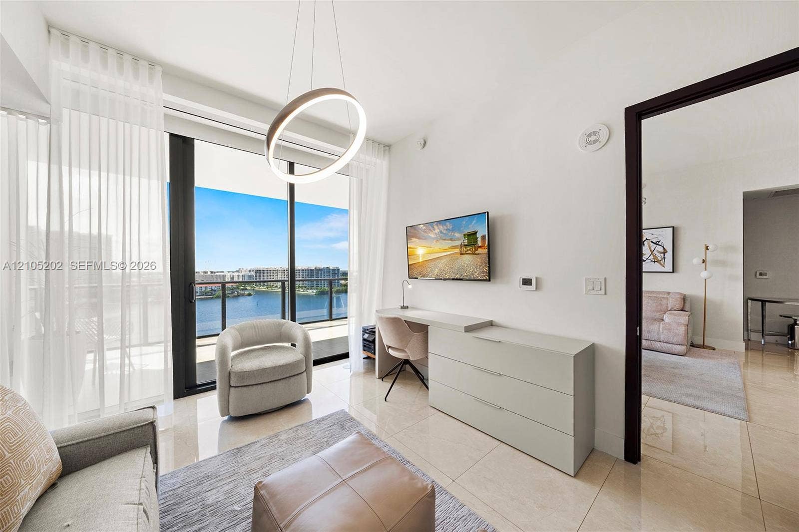 Floor-to-ceiling sliding glass doors, polished tile flooring, circular pendant lighting, and a private balcony overlooking the water