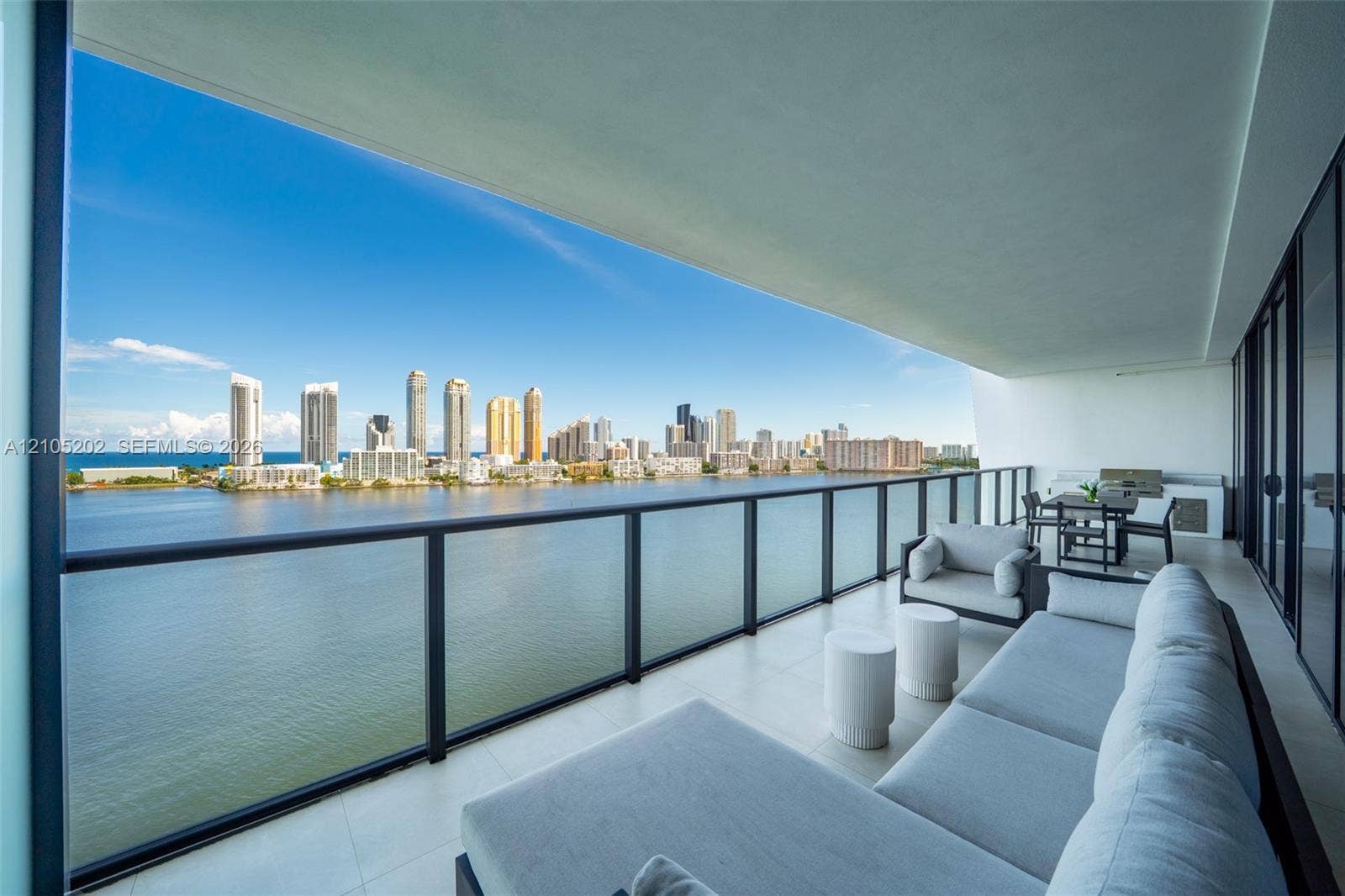 Expansive balcony featuring neutral tile flooring, glass-paneled railing, and built-in outdoor kitchen cabinetry
