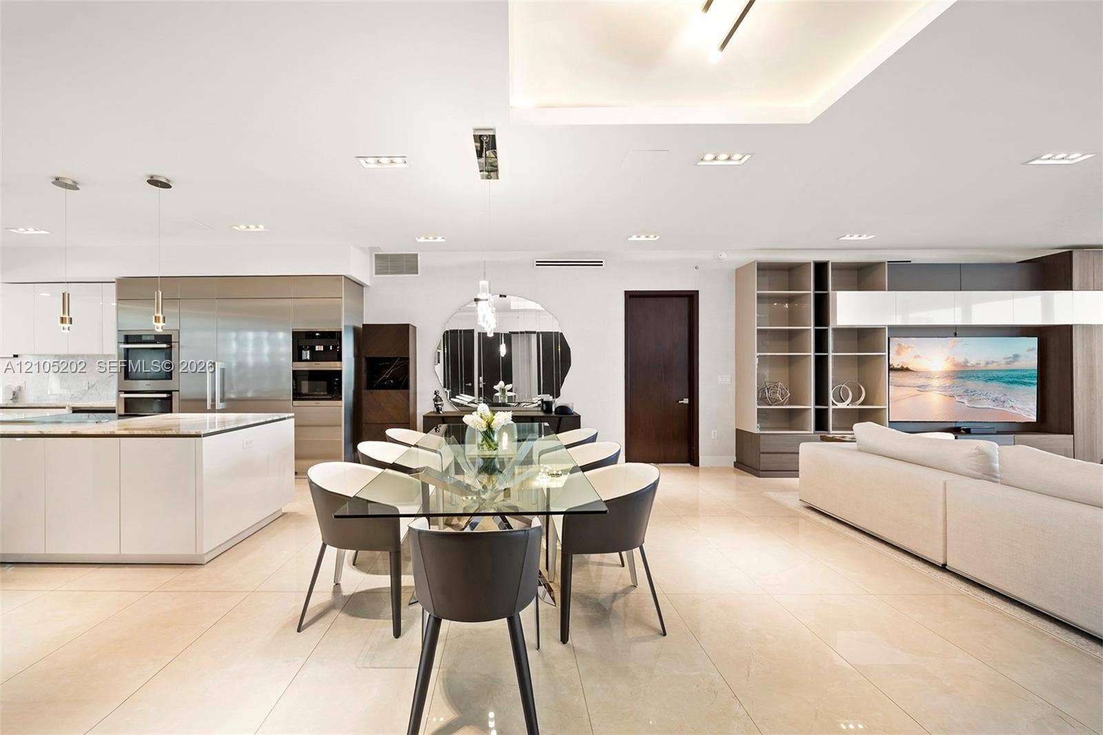 Open-concept living space featuring high-gloss cabinetry, large-format tile flooring, recessed cove lighting, and a custom built-in media shelving unit