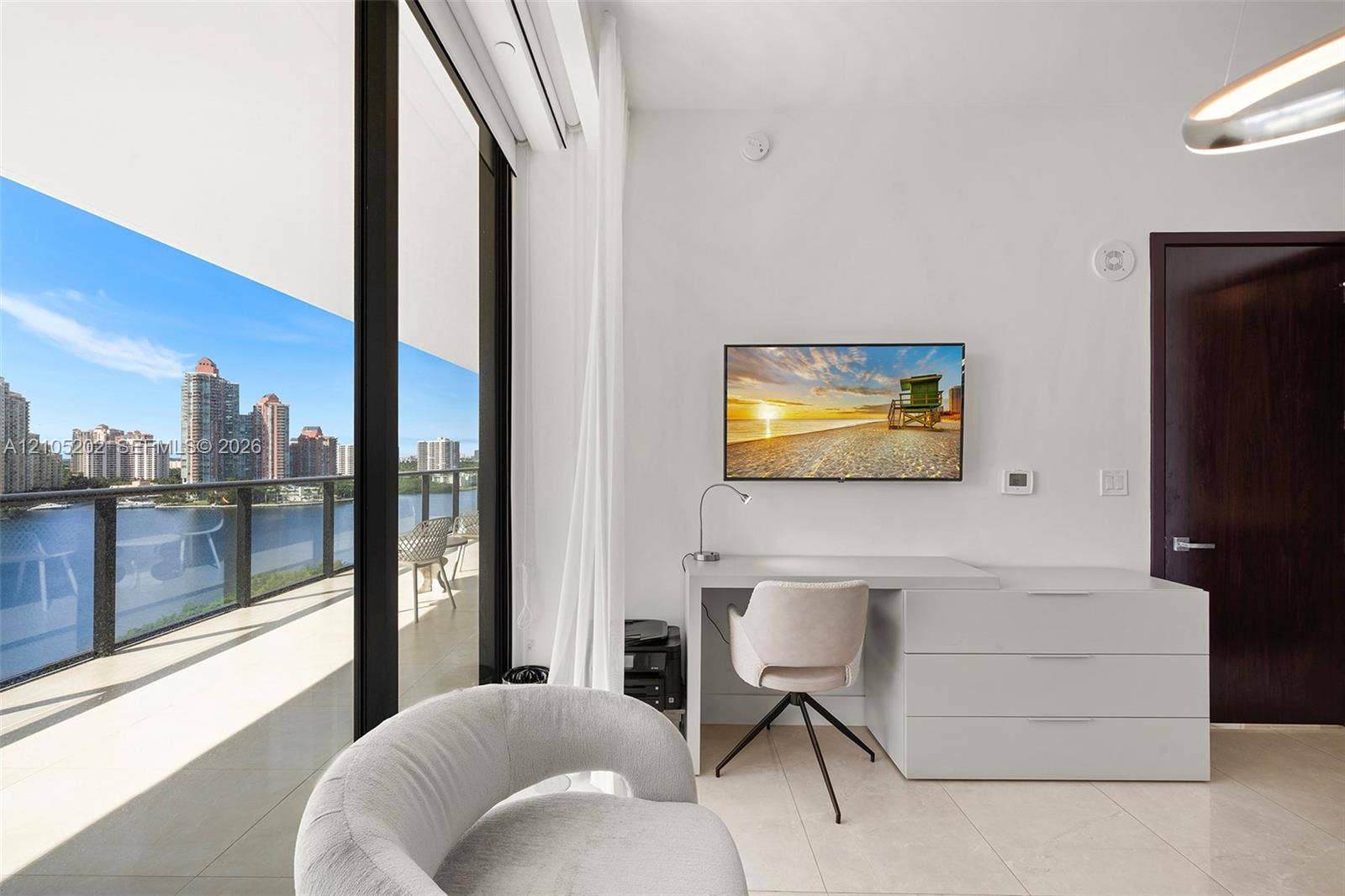 Floor-to-ceiling glass sliding doors opening to a private balcony, polished tile flooring, and custom built-in workstation with integrated drawers