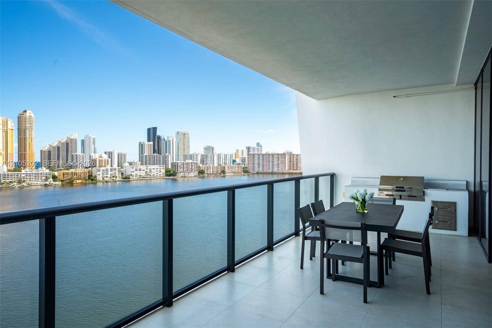 Covered balcony featuring tile flooring, glass-paneled railing, and built-in stainless steel outdoor kitchen components