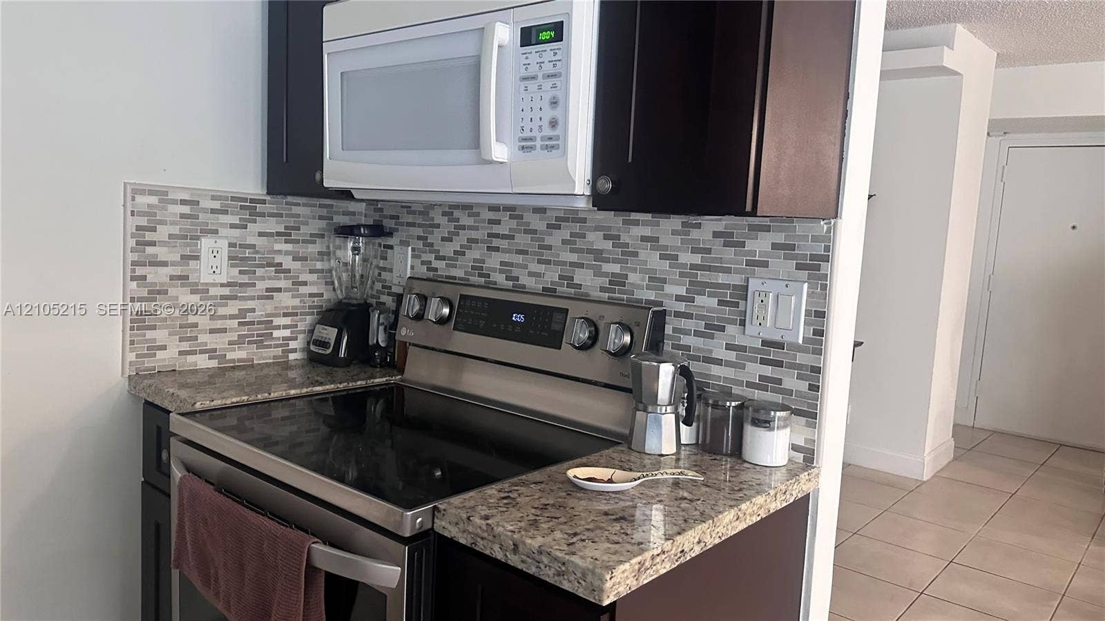 17021 N Bay Road, #114, Sunny Isles Beach, Sunny Isles Beach, FL 33160 Kitchen featuring dark cabinetry, stone-finish countertops, stainless steel range, white over-the-range microwave, and a multicolored glass tile backsplash