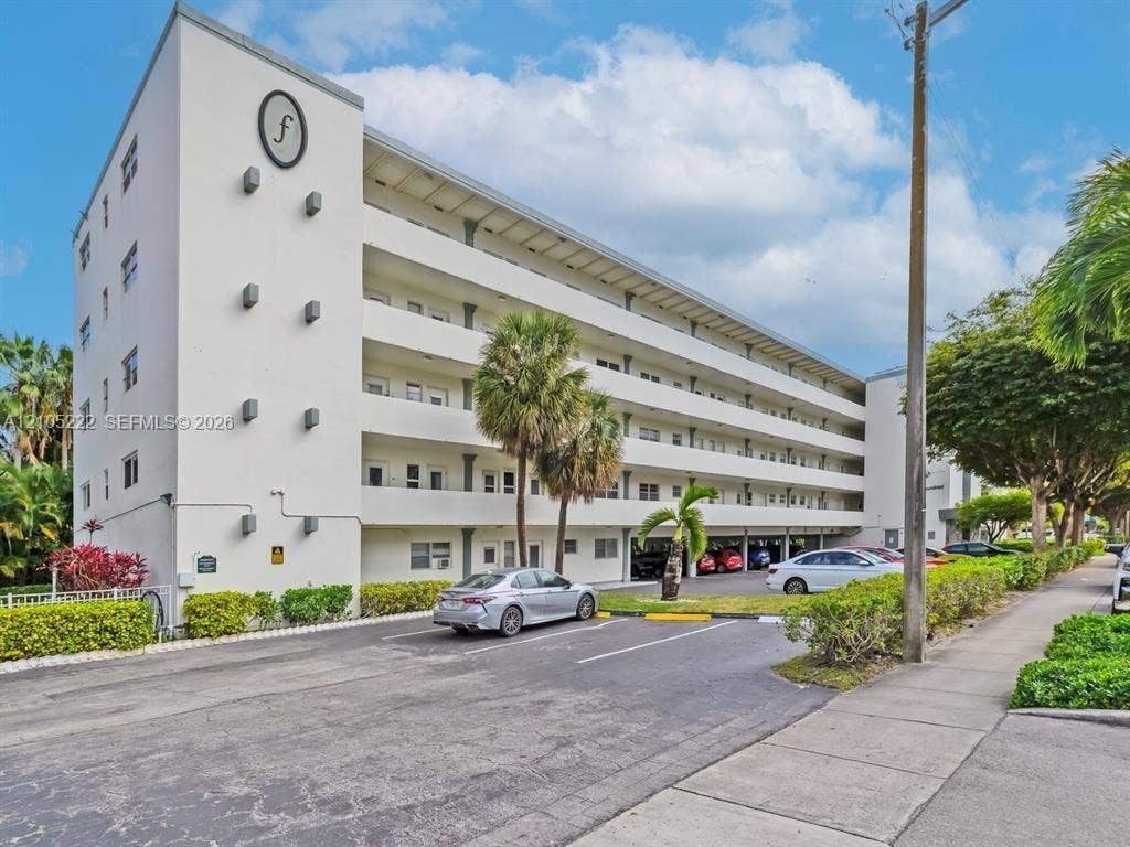 Multi-story concrete exterior featuring covered balcony levels, column supports, and ground-level parking