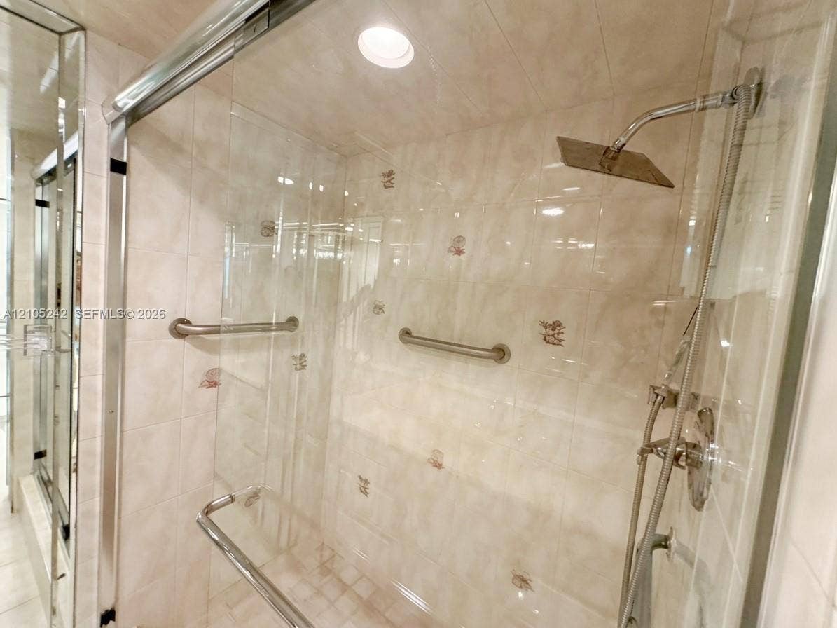 Glass-enclosed shower with a rainfall showerhead, handheld shower fixture, and polished chrome grab bars