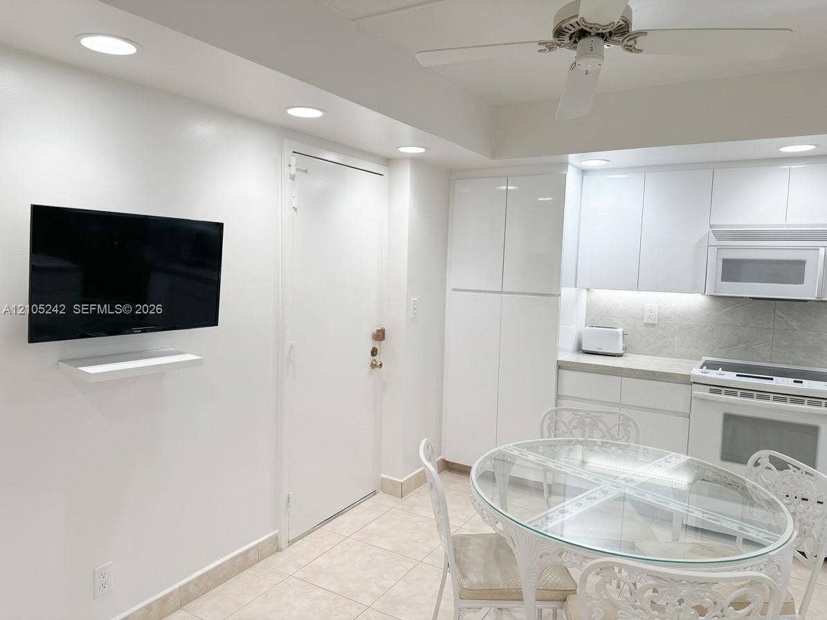 Recessed lighting, white high-gloss cabinetry, tiled flooring, integrated oven and microwave, and a ceiling fan with light fixture