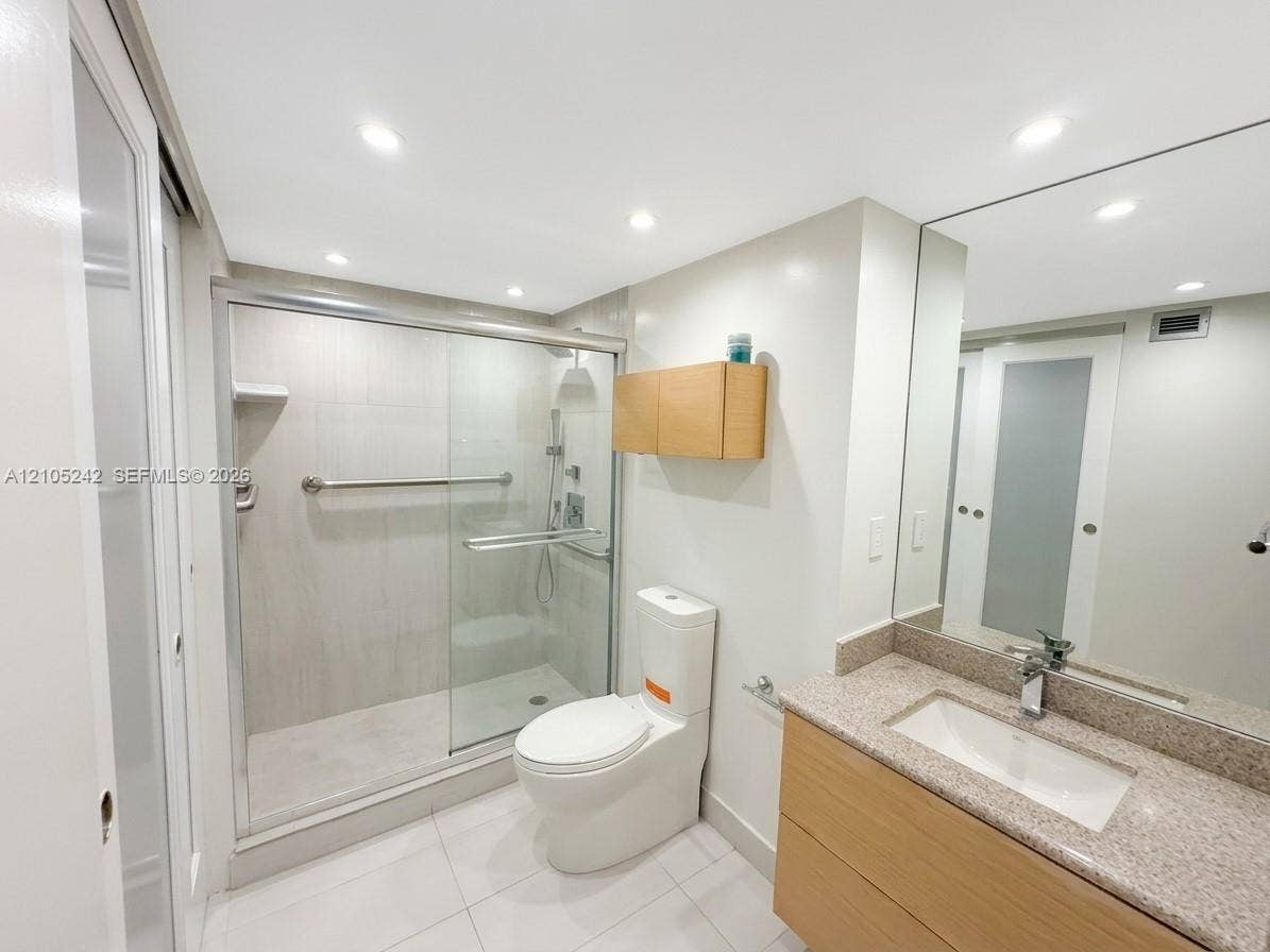 Shower with sliding glass enclosure, wood-finish vanity with an integrated sink, granite-patterned countertop, and large wall-mounted mirror