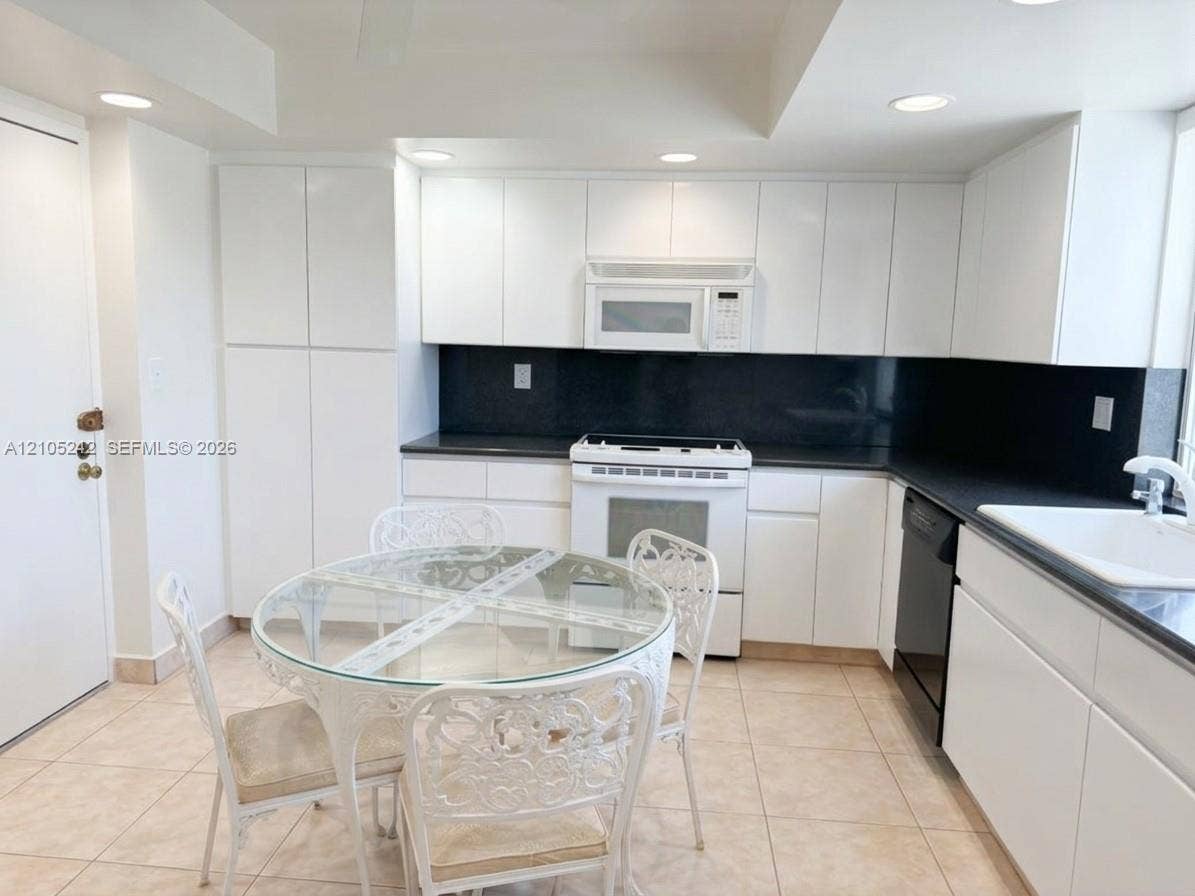 Kitchen featuring white cabinetry, dark countertops, tile flooring, and integrated white appliances
