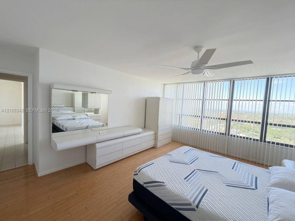 Floor-to-ceiling windows with vertical blinds, wood-finish flooring, and a ceiling fan