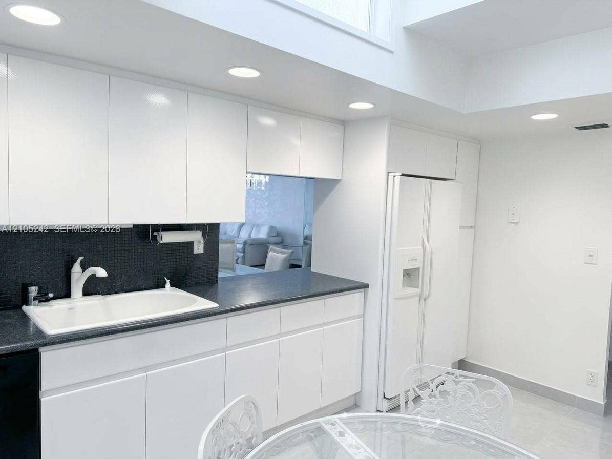 White cabinetry with integrated handles, dark countertops, a white double-basin sink, and recessed lighting