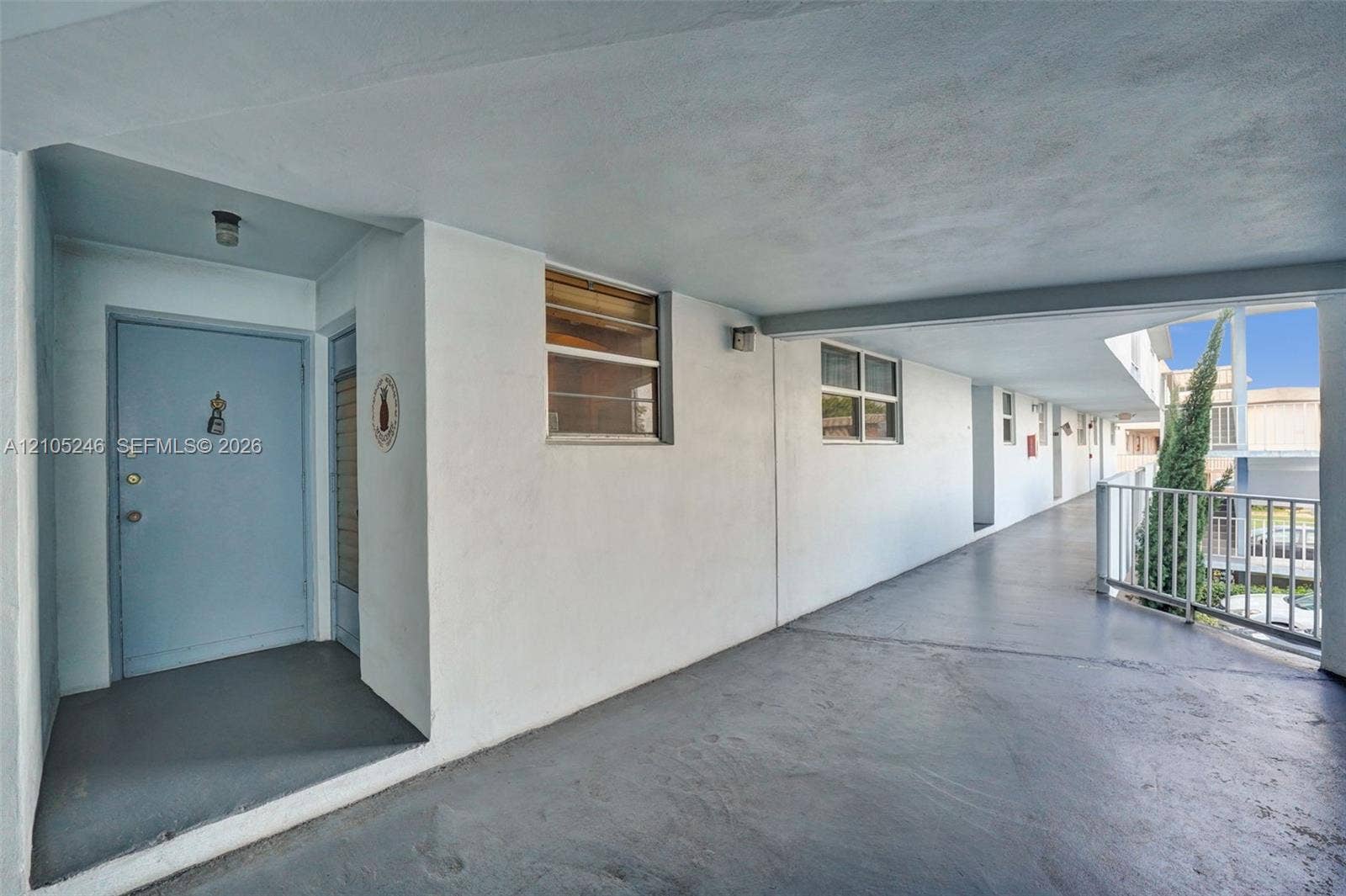 1400 Tallwood Avenue, #207, Hollywood, FL 33021 Exterior walkway featuring smooth stucco walls, solid-core entrance door, recessed overhead lighting, and white metal railings