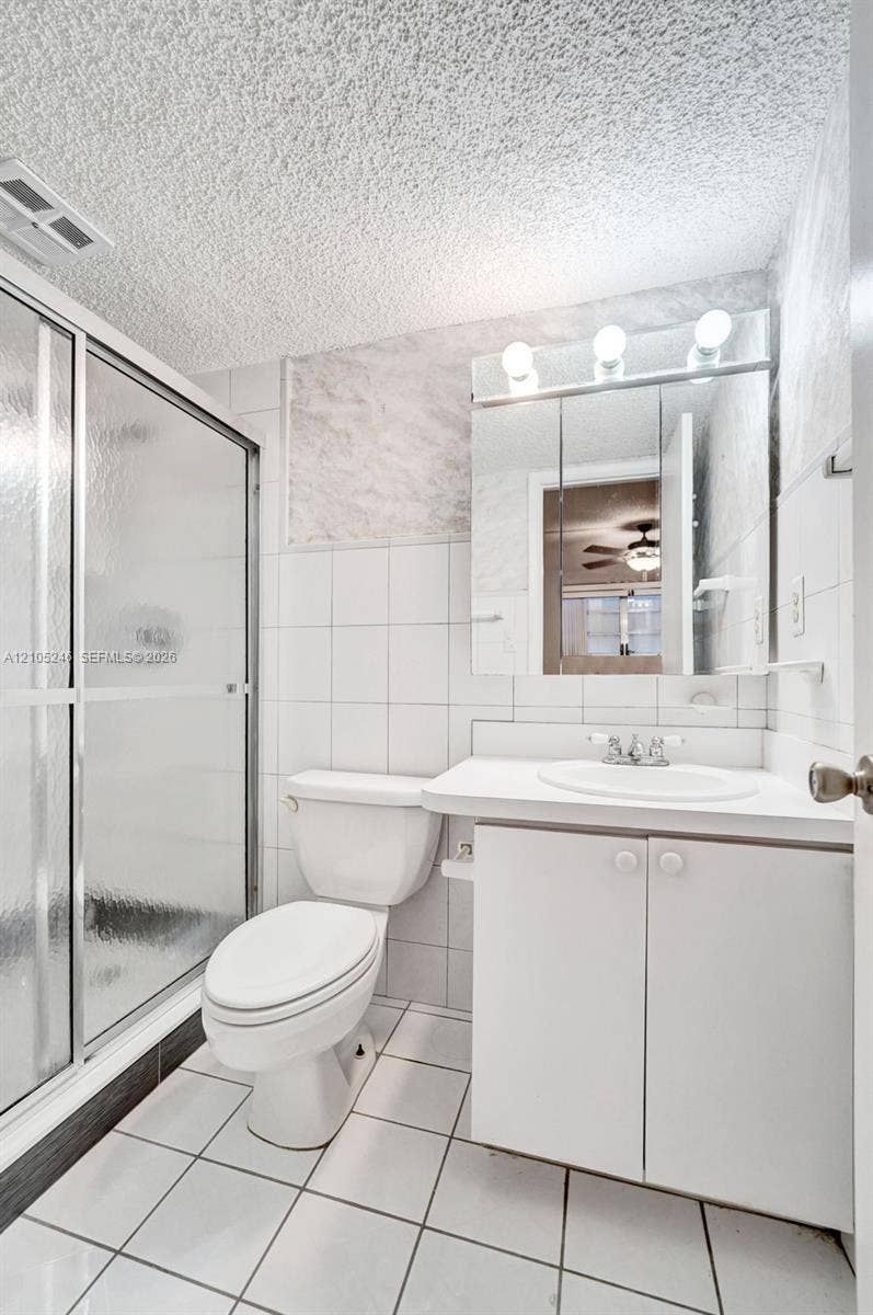 1400 Tallwood Avenue, #207, Hollywood, FL 33021 Bathroom featuring a walk-in shower with metal-framed glass doors, white tiled walls, a vanity with a white countertop and integrated sink, and a triple-light fixture above a mirrored cabinet