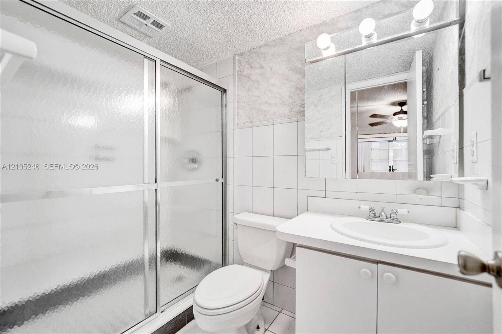 1400 Tallwood Avenue, #207, Hollywood, FL 33021 Bathroom featuring a shower with a textured glass sliding door, integrated vanity with a basin sink, expansive wall-mounted mirror, and wall-mounted light fixture