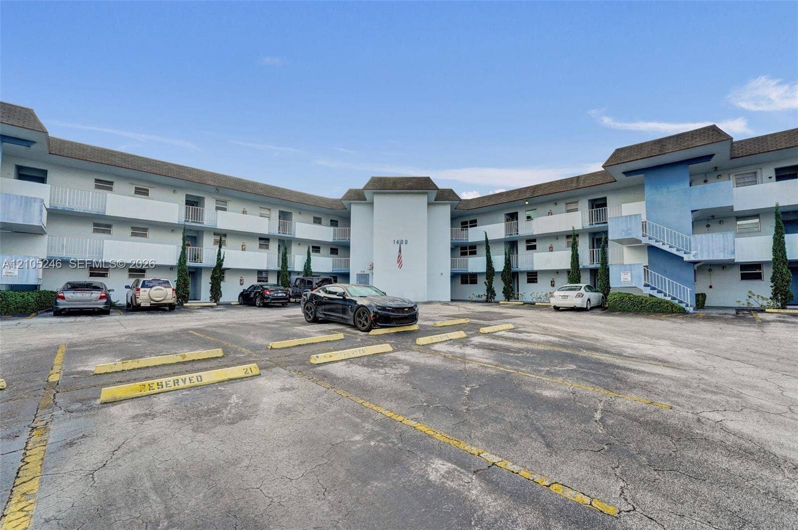 1400 Tallwood Avenue, #207, Hollywood, FL 33021 Multi-story apartment building exterior featuring paved surface parking, covered exterior corridors, and vertical landscaping accents