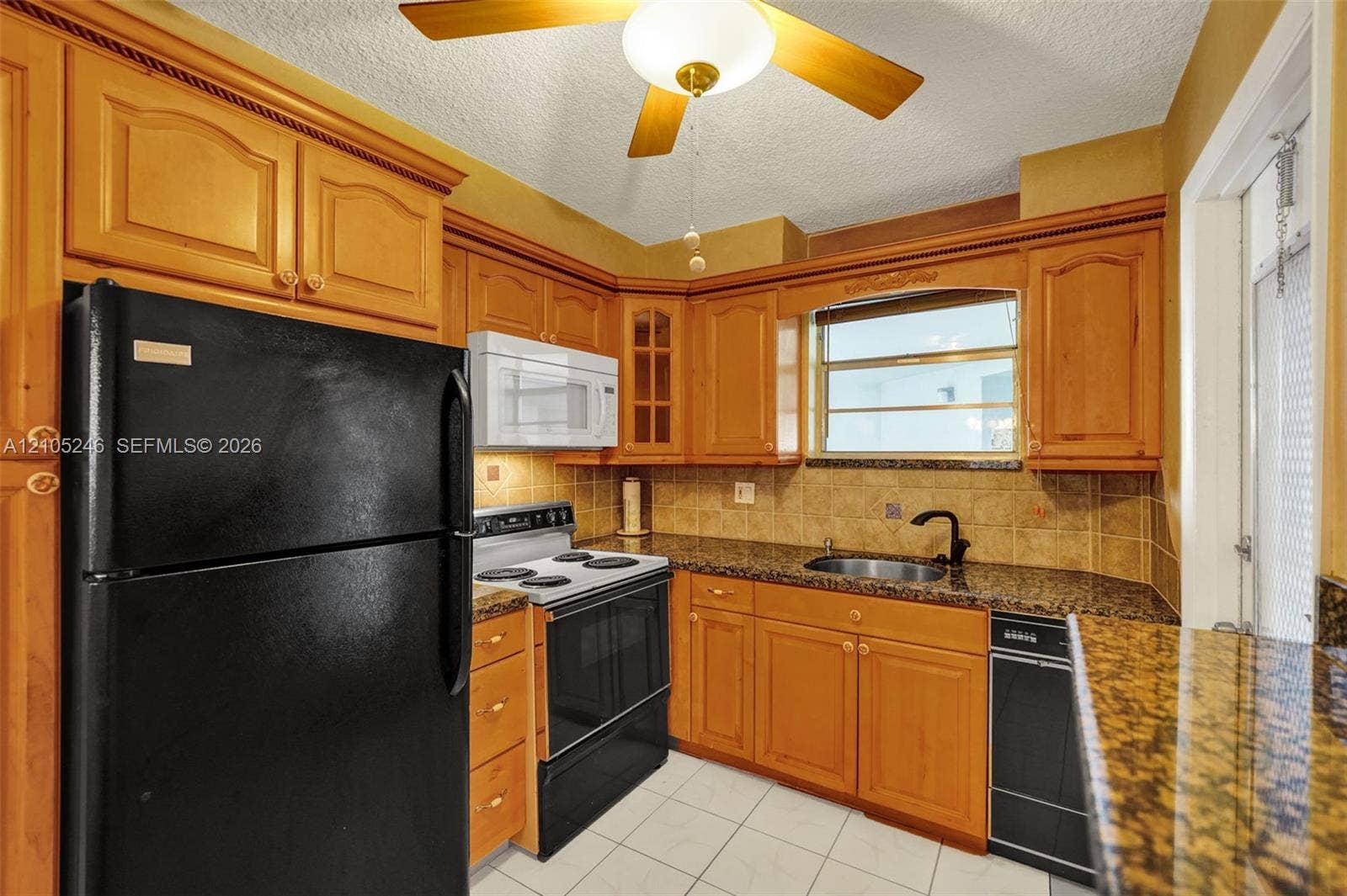1400 Tallwood Avenue, #207, Hollywood, FL 33021 Kitchen featuring wood cabinetry, stone countertops, a tile backsplash, tile flooring, and integrated black appliances