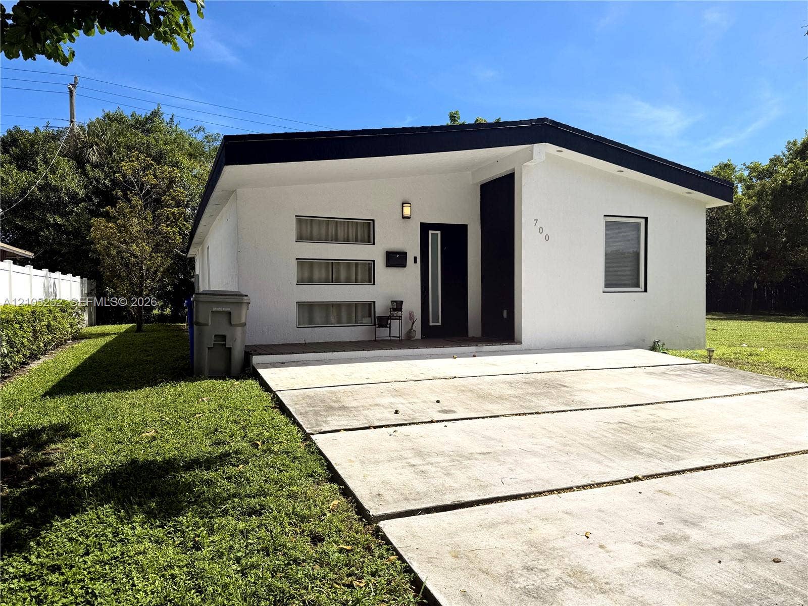 700 NW 17th Terrace, Pompano Beach, FL 33069 White stucco exterior with black trim, modern entry door, concrete panel driveway, and a white fence