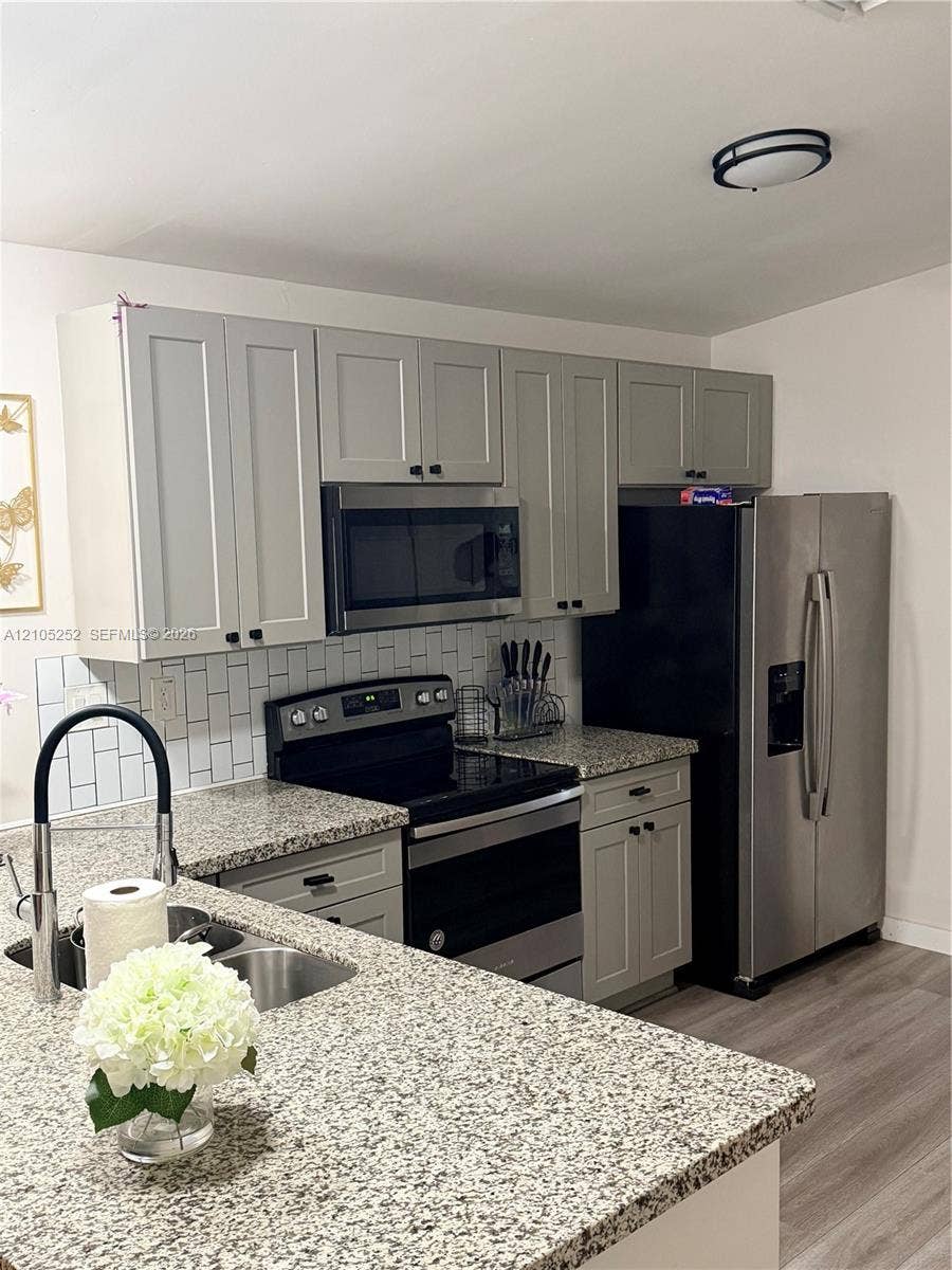 700 NW 17th Terrace, Pompano Beach, FL 33069 Updated kitchen featuring granite countertops, stainless steel appliances, light gray shaker cabinetry, a subway tile backsplash, and wood-finish flooring