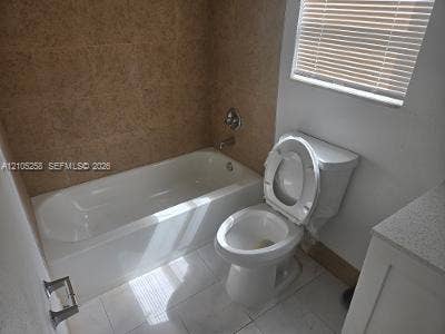 2208 Garfield Street, #B, Hollywood, Hollywood, FL 33020 White bathtub with chrome fixtures, tiled shower surround, white toilet, white tile flooring, and a window with blinds