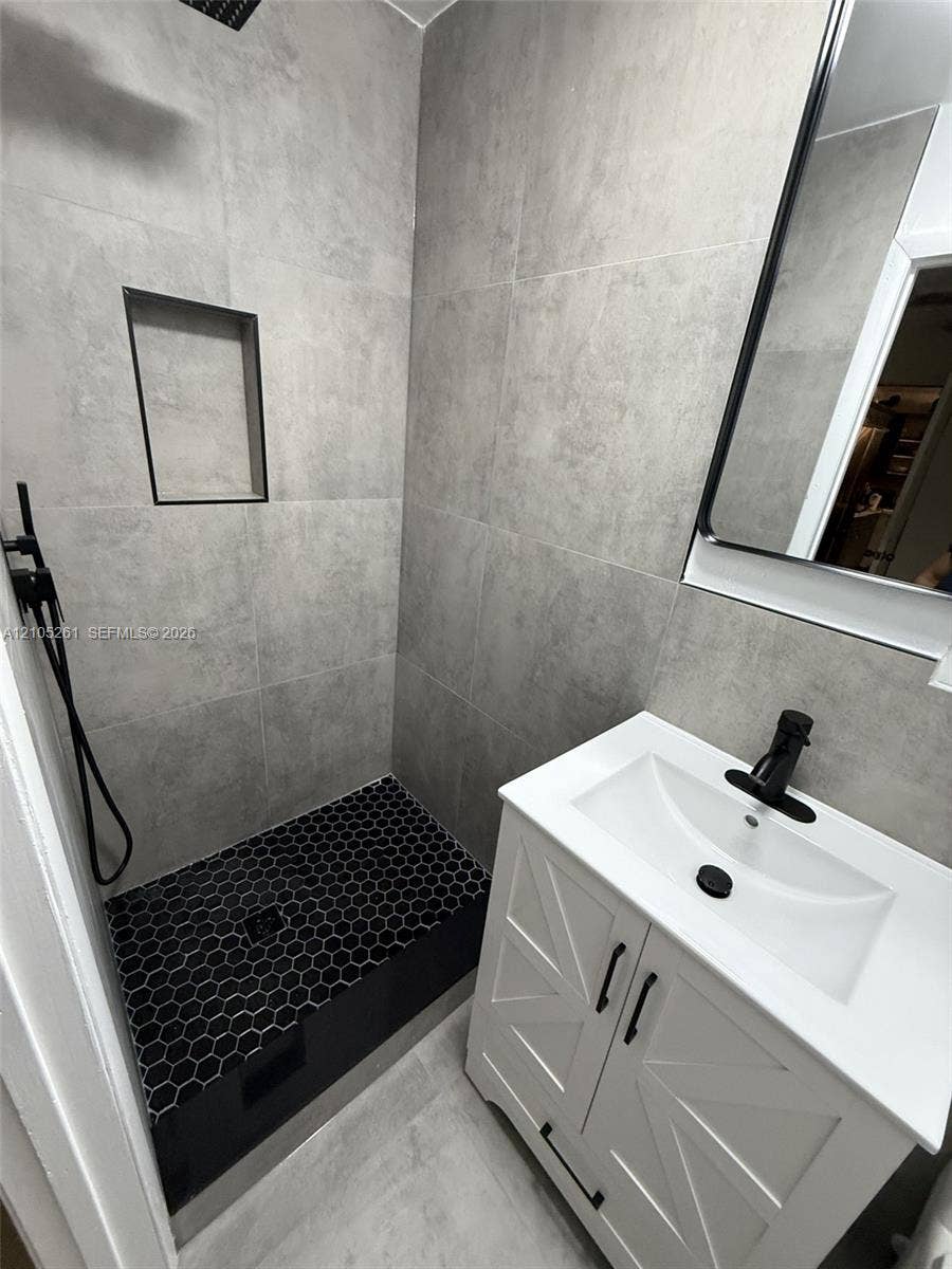 Tiled shower with a recessed niche, black hexagon tile flooring, and a rainfall showerhead