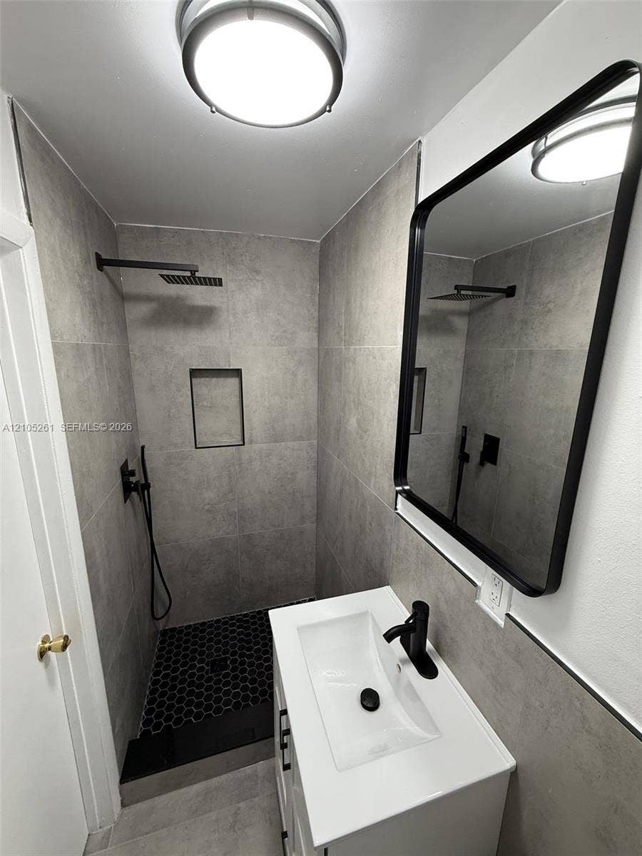 Tiled shower with a rainfall showerhead, recessed niche, and black hexagonal floor tiles