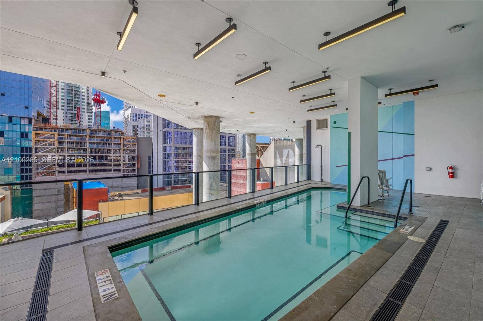 398 NE 5th Street, #2219, Miami, FL 33132 Covered swimming pool featuring linear overhead lighting, structured support columns, and stone-tile decking with integrated drainage