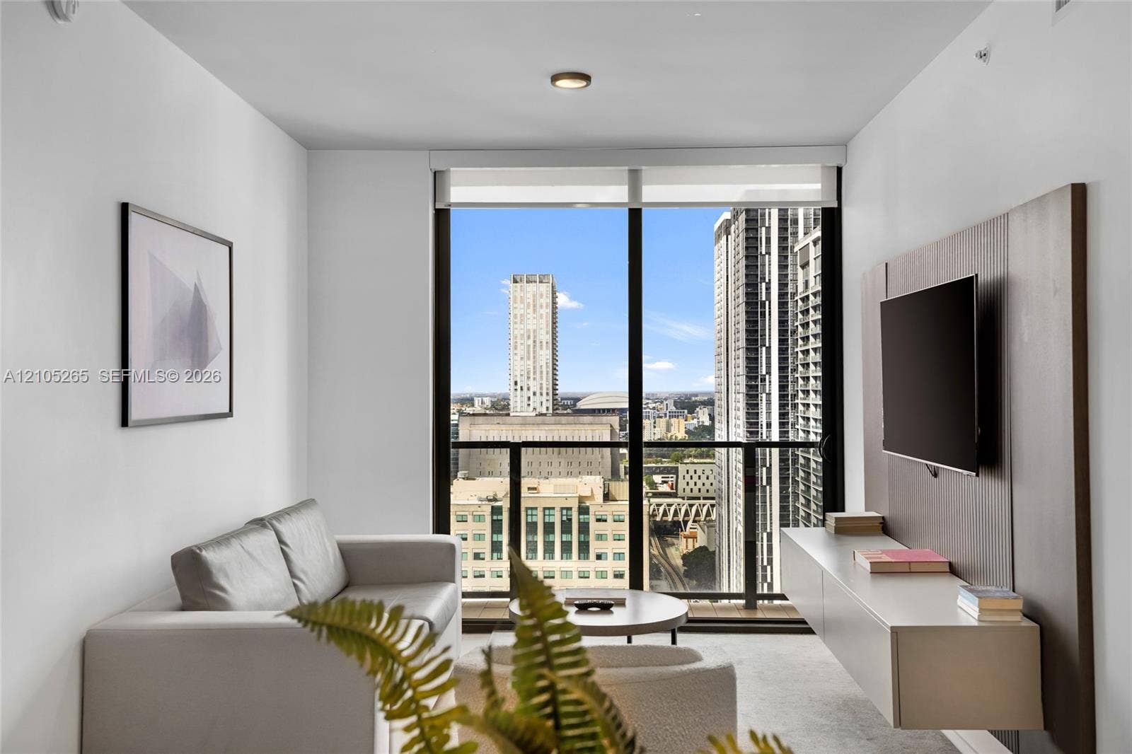 398 NE 5th Street, #2219, Miami, FL 33132 Floor-to-ceiling windows, integrated wall-mounted media console with wood-finish paneling, and private balcony with urban skyline scenery